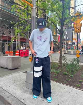 Paul Soles standing on a city street wearing a light gray t-shirt, kayoz naruto shinobi cargos, and a cap.