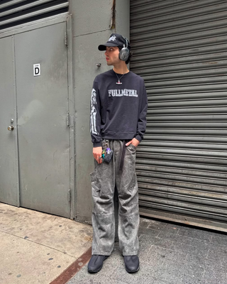 Person wearing a 'Fullmetal' sweatshirt and gray pants standing against a metal shutter.